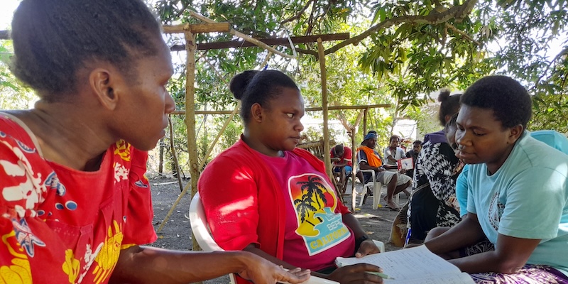 Indigenous women in Vanuatu engaged in a group discussion during an outdoor community training session.