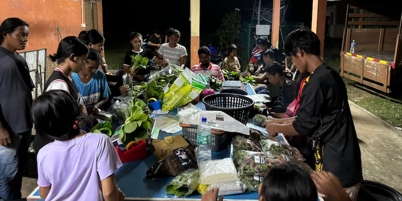 Farmers gather around a table to pack their harvests in Malaysia.