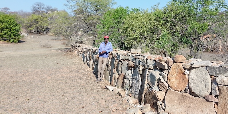A man stands next to the dry stone wall in Zimbabwe.