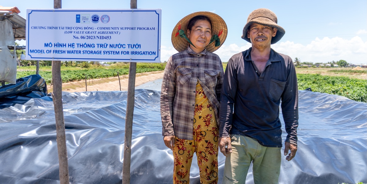 A man and a woman stand next to a sign of the project in their farm in Viet Nam