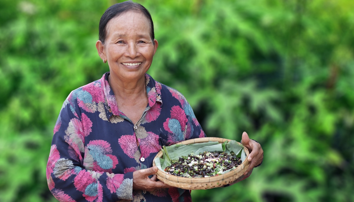 A woman smiling shows a basket of crickets in Cambodia.