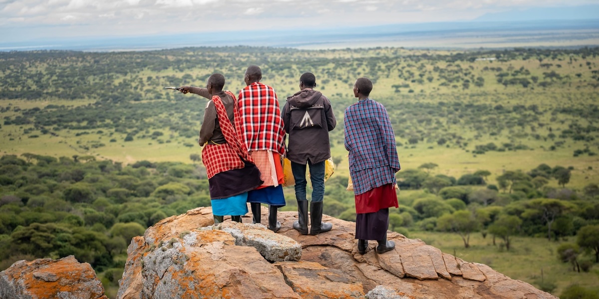 Four people standing on a mountain rock observe the view of land in Tanzania.