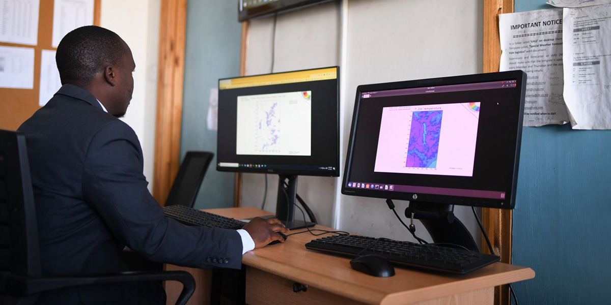 A meteorological officer in Malawi analyzes digital climate and temperature maps on dual computer screens to support early warning and climate information services.