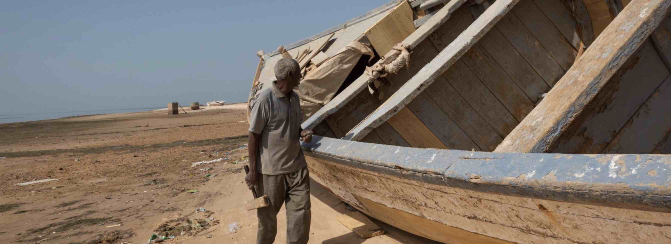 Man walking next to grounded boat on beach in Tanzania 
