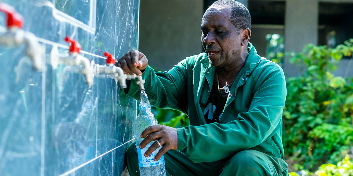 A man fills a plastic bottle from a row of outdoor water taps in Comoros